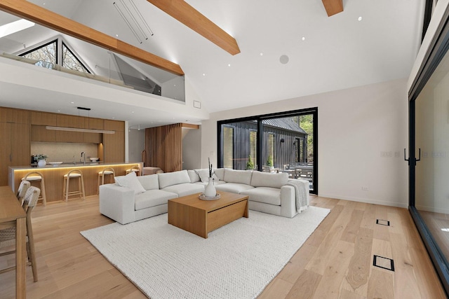 living area with high vaulted ceiling, beam ceiling, light wood-style flooring, and baseboards