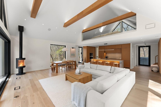 living area featuring high vaulted ceiling, beam ceiling, light wood finished floors, plenty of natural light, and a wood stove