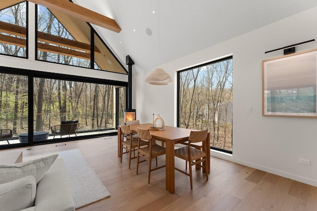 dining room with high vaulted ceiling, healthy amount of natural light, baseboards, wood finished floors, and a wood stove
