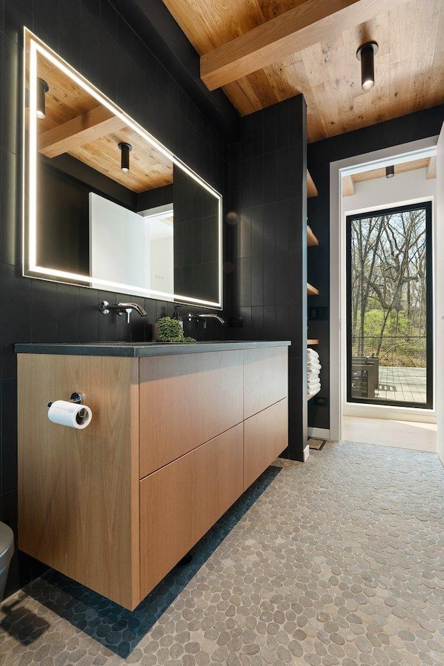 bathroom featuring wood ceiling, double vanity, beam ceiling, stone finish flooring, and toilet