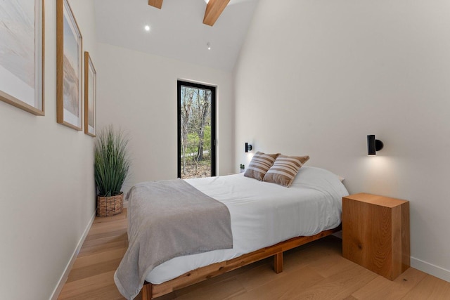 bedroom featuring baseboards, light wood-style floors, a skylight, ceiling fan, and high vaulted ceiling