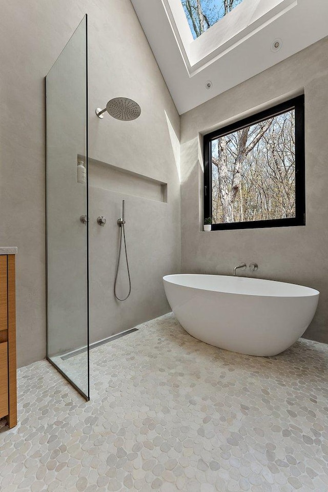 bathroom with stone flooring, a skylight, a walk in shower, a freestanding tub, and a towering ceiling