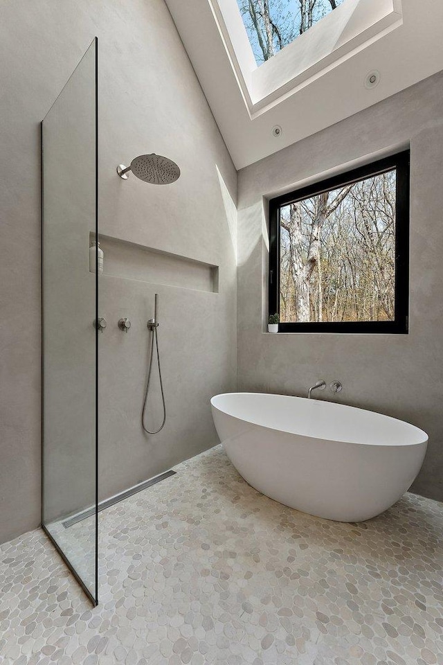 bathroom featuring stone floors, walk in shower, a skylight, a soaking tub, and a towering ceiling