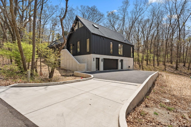 view of side of property featuring driveway, metal roof, a standing seam roof, an attached garage, and board and batten siding