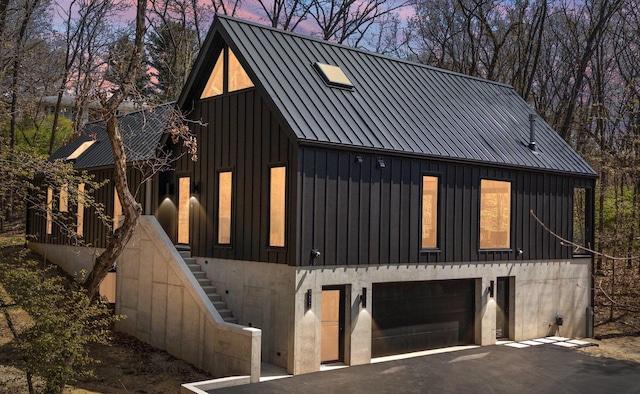 modern farmhouse featuring stairs, driveway, a garage, board and batten siding, and metal roof
