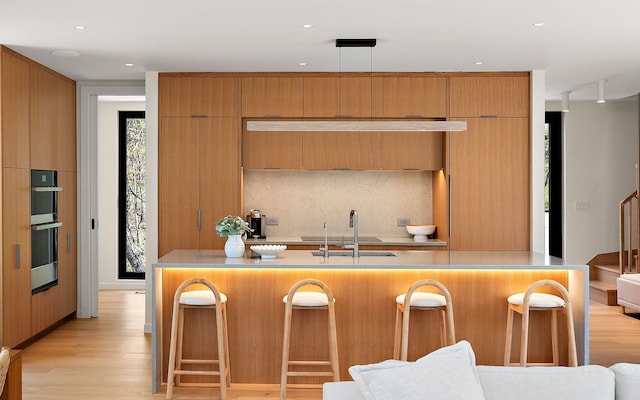kitchen featuring a sink, a kitchen breakfast bar, decorative backsplash, light wood-style flooring, and recessed lighting