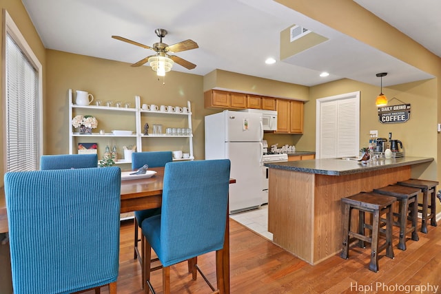 kitchen with a peninsula, dark countertops, white appliances, light wood-style floors, and ceiling fan