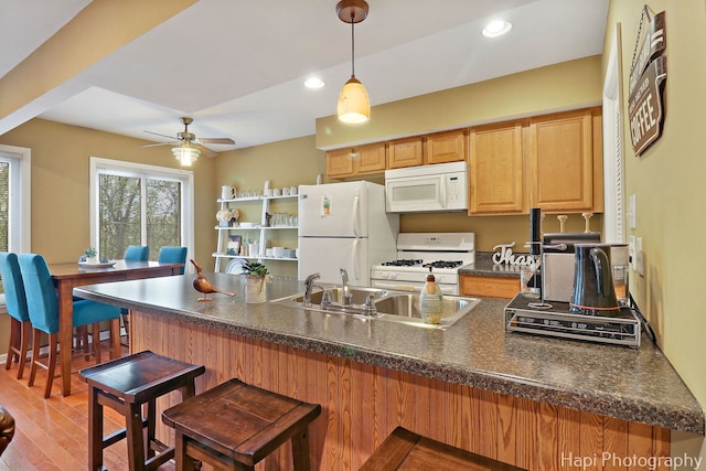 kitchen with dark countertops, a sink, a peninsula, a breakfast bar, and white appliances