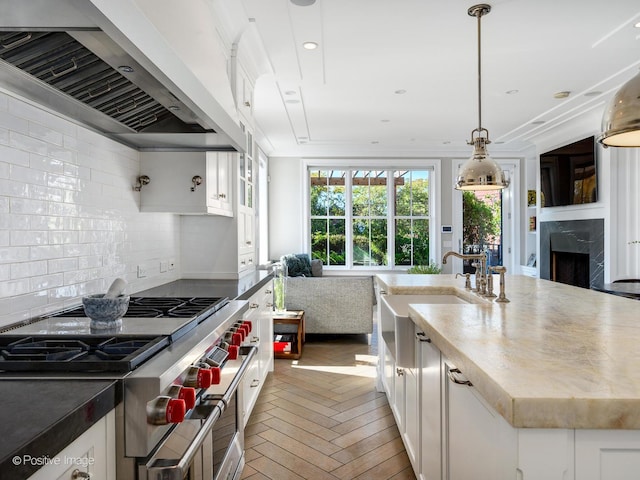 kitchen with decorative backsplash, open floor plan, wall chimney exhaust hood, white cabinetry, and range with two ovens