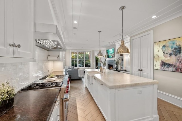 kitchen with backsplash, a sink, white cabinets, a warm lit fireplace, and range with gas stovetop