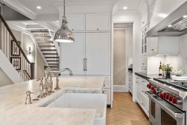 kitchen featuring wall chimney range hood, range with two ovens, hanging light fixtures, a sink, and white cabinetry