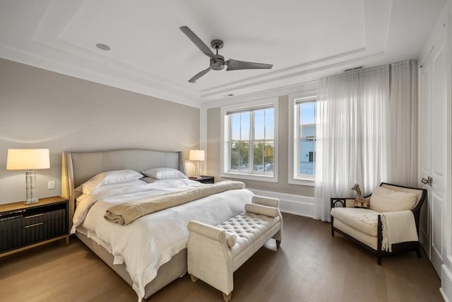 bedroom with light wood-style flooring, a raised ceiling, and a ceiling fan