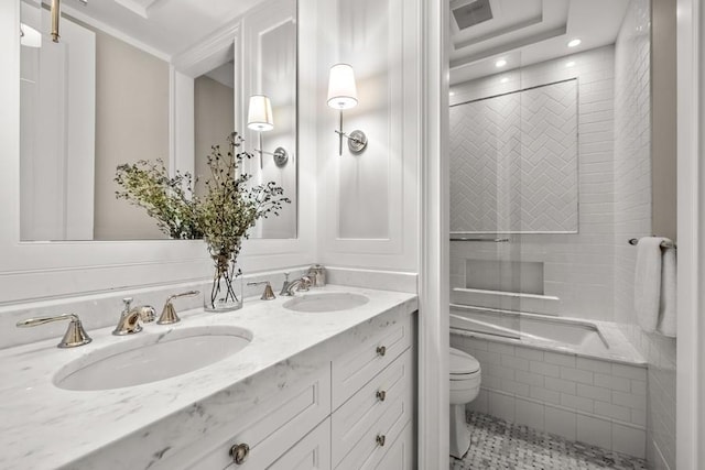 bathroom featuring double vanity, a sink, tiled shower / bath, and toilet