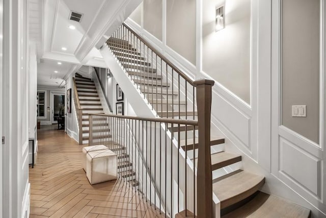 stairs featuring visible vents, crown molding, wainscoting, a decorative wall, and recessed lighting