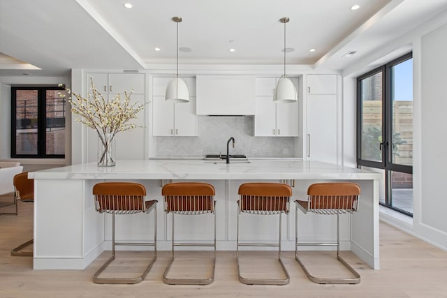 kitchen with a sink, white cabinetry, light wood finished floors, and tasteful backsplash