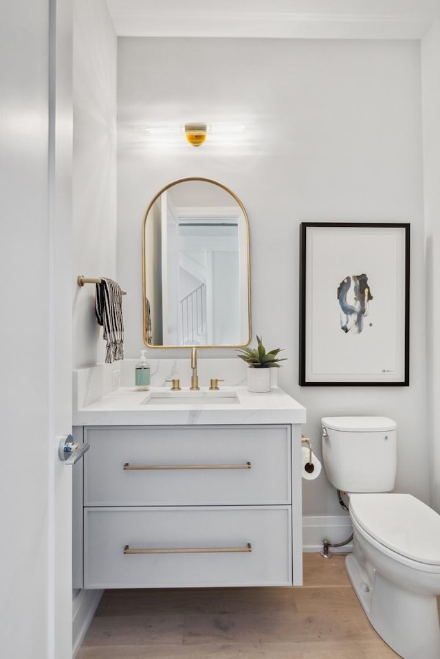 half bath featuring vanity, baseboards, toilet, and wood finished floors