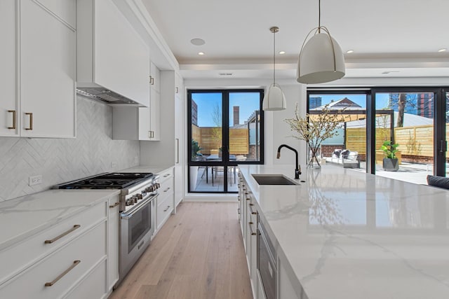 kitchen featuring light wood-type flooring, white cabinetry, high end stove, a sink, and backsplash