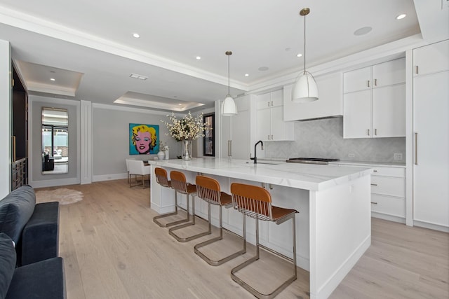 kitchen featuring decorative backsplash, white cabinetry, a sink, a tray ceiling, and light wood-style flooring