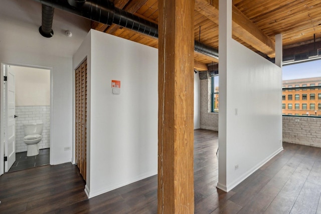 corridor with beam ceiling, wood finished floors, brick wall, tile walls, and wooden ceiling