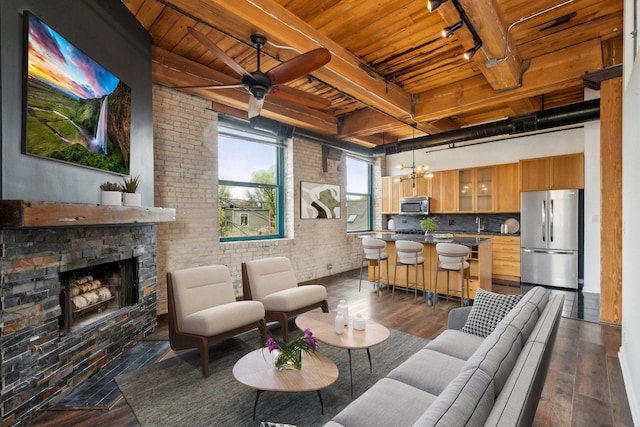 living area with beam ceiling, a stone fireplace, wood ceiling, and dark wood-type flooring