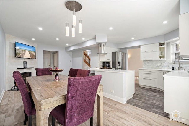 dining room with light wood-style flooring, stairs, recessed lighting, and a large fireplace