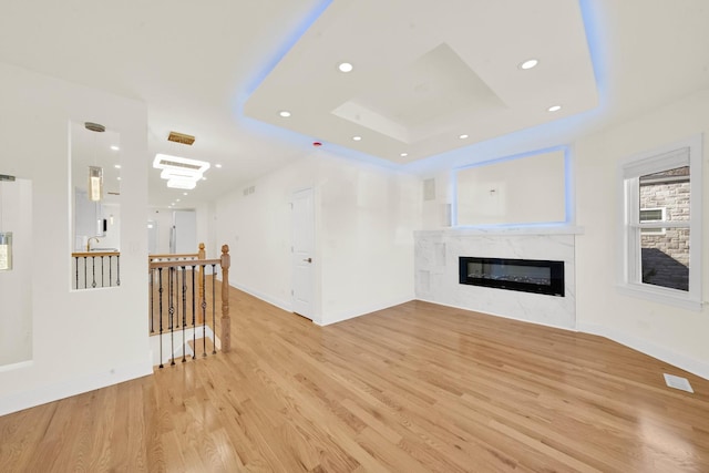 unfurnished living room featuring visible vents, a glass covered fireplace, light wood-style floors, baseboards, and a tray ceiling
