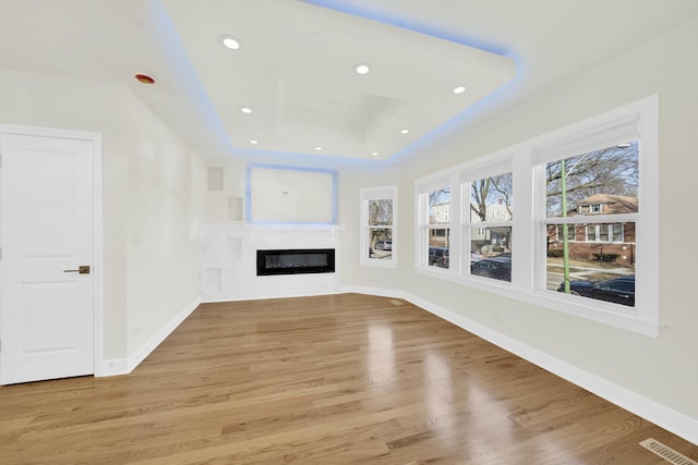 unfurnished living room featuring a glass covered fireplace, baseboards, a tray ceiling, and visible vents