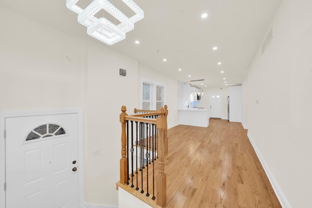 hallway with an inviting chandelier, visible vents, recessed lighting, light wood finished floors, and an upstairs landing