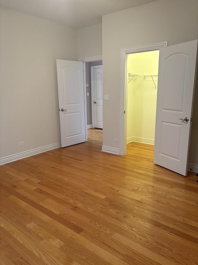 unfurnished bedroom with light wood finished floors, a walk in closet, baseboards, and a closet