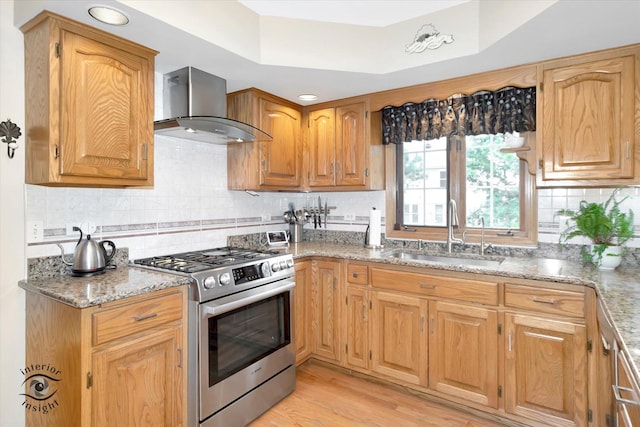 kitchen featuring wall chimney range hood, stainless steel range with gas stovetop, tasteful backsplash, a sink, and light stone counters