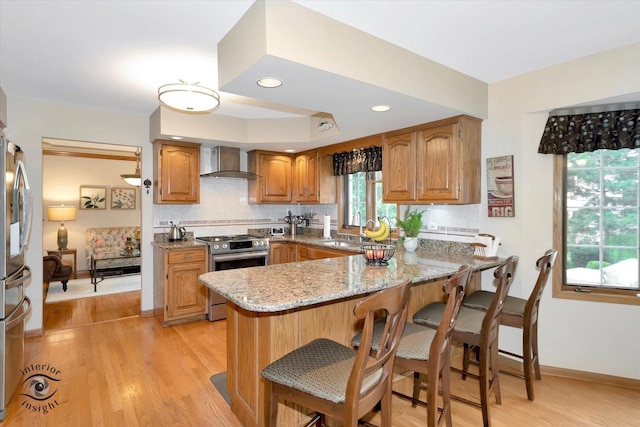 kitchen featuring stainless steel range with electric cooktop, a sink, light stone counters, a peninsula, and wall chimney exhaust hood