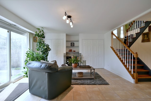 living room with light tile patterned floors, baseboards, a fireplace, and stairs