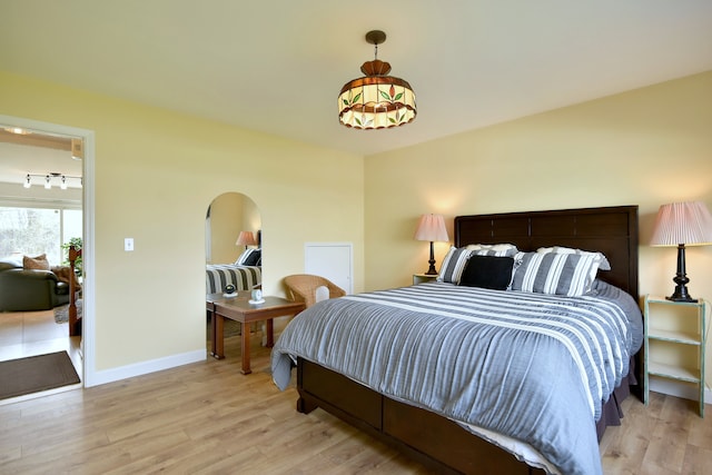 bedroom featuring baseboards, arched walkways, and light wood-style flooring