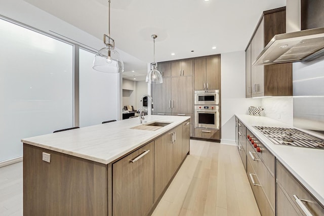 kitchen featuring a kitchen island with sink, stainless steel oven, modern cabinets, wall chimney range hood, and a sink
