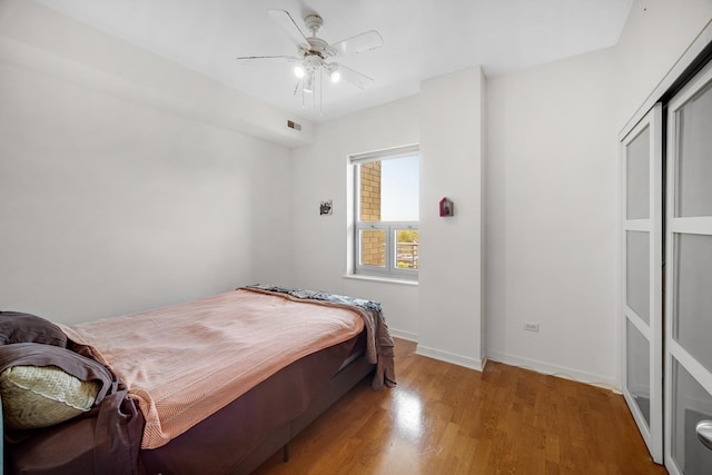 bedroom with baseboards, a ceiling fan, wood finished floors, and visible vents