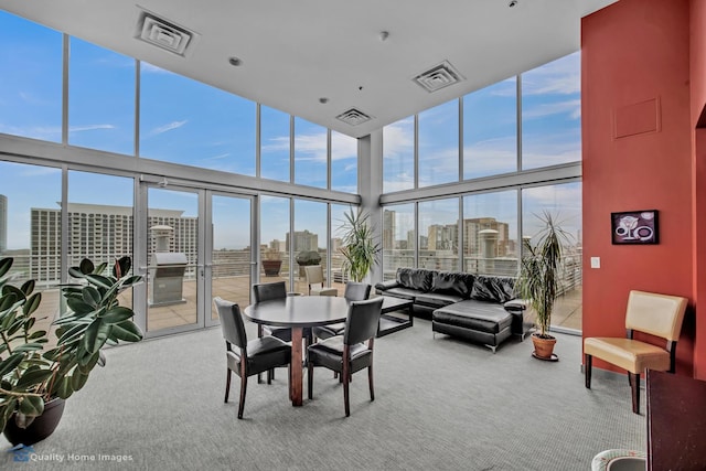 interior space with visible vents, a towering ceiling, expansive windows, a view of city, and carpet flooring
