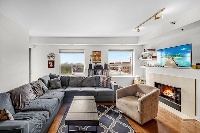 living room with track lighting, plenty of natural light, wood finished floors, and a tile fireplace