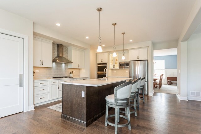 kitchen featuring an island with sink, white cabinetry, visible vents, wall chimney range hood, and appliances with stainless steel finishes