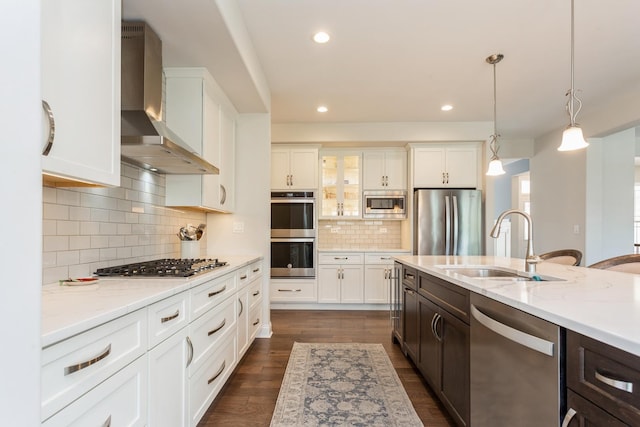 kitchen featuring white cabinetry, wall chimney range hood, stainless steel appliances, and a sink