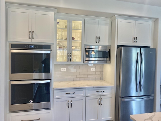 kitchen featuring decorative backsplash, white cabinets, appliances with stainless steel finishes, and glass insert cabinets