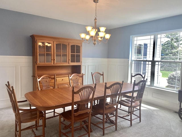 dining area featuring light carpet, a notable chandelier, a decorative wall, and wainscoting