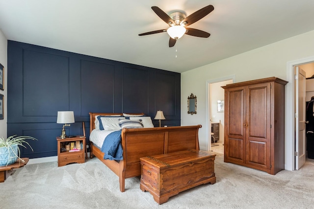 bedroom with light carpet, ensuite bath, a decorative wall, and ceiling fan