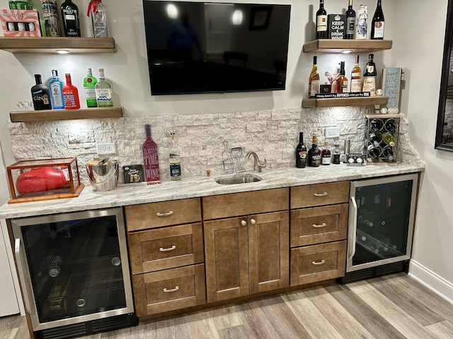 bar featuring a sink, light wood-type flooring, beverage cooler, and indoor wet bar