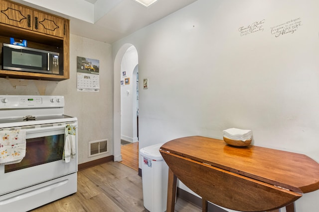 kitchen with electric stove, stainless steel microwave, arched walkways, brown cabinetry, and light wood-style flooring