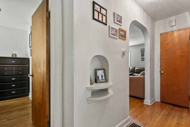 hallway featuring wood finished floors, arched walkways, and baseboards
