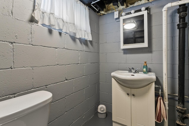 bathroom featuring vanity, toilet, and concrete block wall