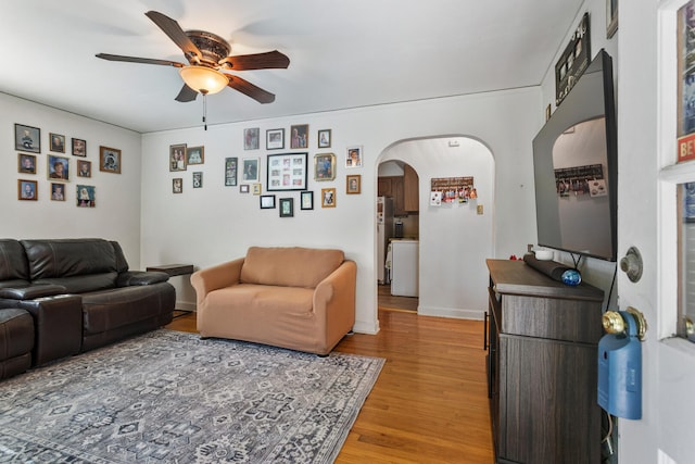 living area with ceiling fan, arched walkways, light wood-type flooring, and baseboards