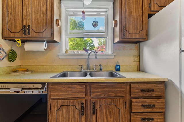 kitchen with dishwasher, a sink, freestanding refrigerator, and light countertops