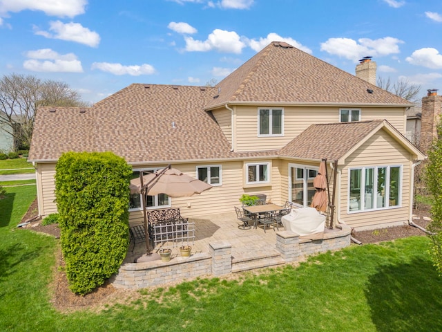 rear view of property featuring a lawn, a patio area, a shingled roof, and a chimney