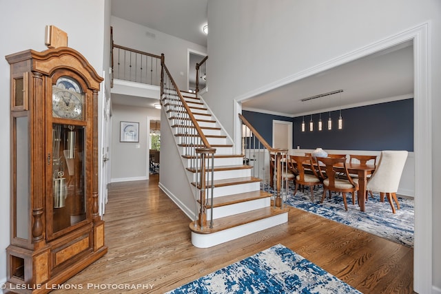 staircase featuring wood finished floors, baseboards, and a high ceiling
